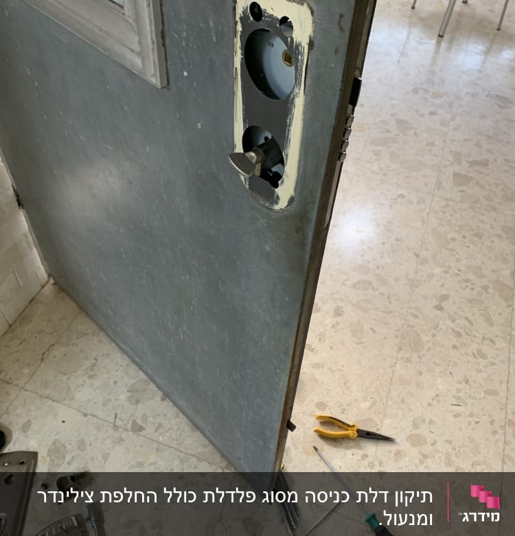דלת פתוחה עם חור למנעול, מברג ופלייר על הרצפה